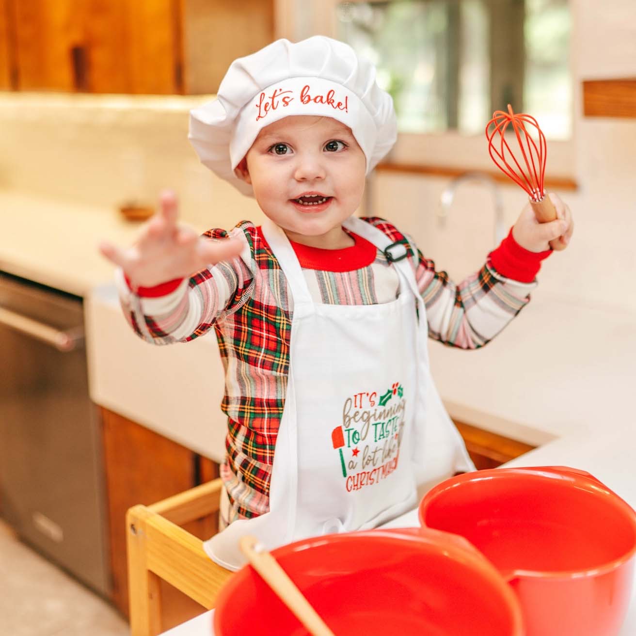elf prop, baking, kitching, kids apron and chef hat, Child in a kitchen wearing a chef's hat and apron, holding a whisk.