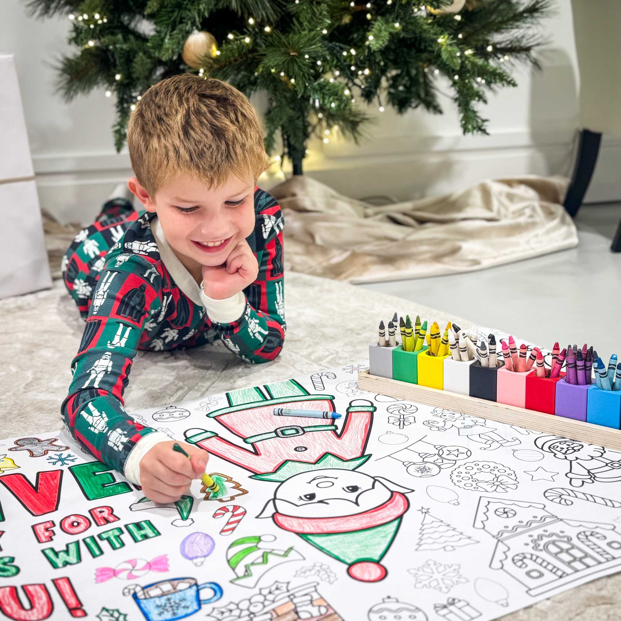 Complement your Elf Kit 2025 with an Elf Arrival Giant Coloring Banner so your elf doesn’t just sit on the shelf. This Elf Arrival Banner is full of magic, christmas themes to make your elf's arrival grand adventure.  Check out our shop for a fun elfin adventures while waiting around for Santa in December!  Child coloring a Christmas-themed picture with crayons in front of a decorated Christmas tree.